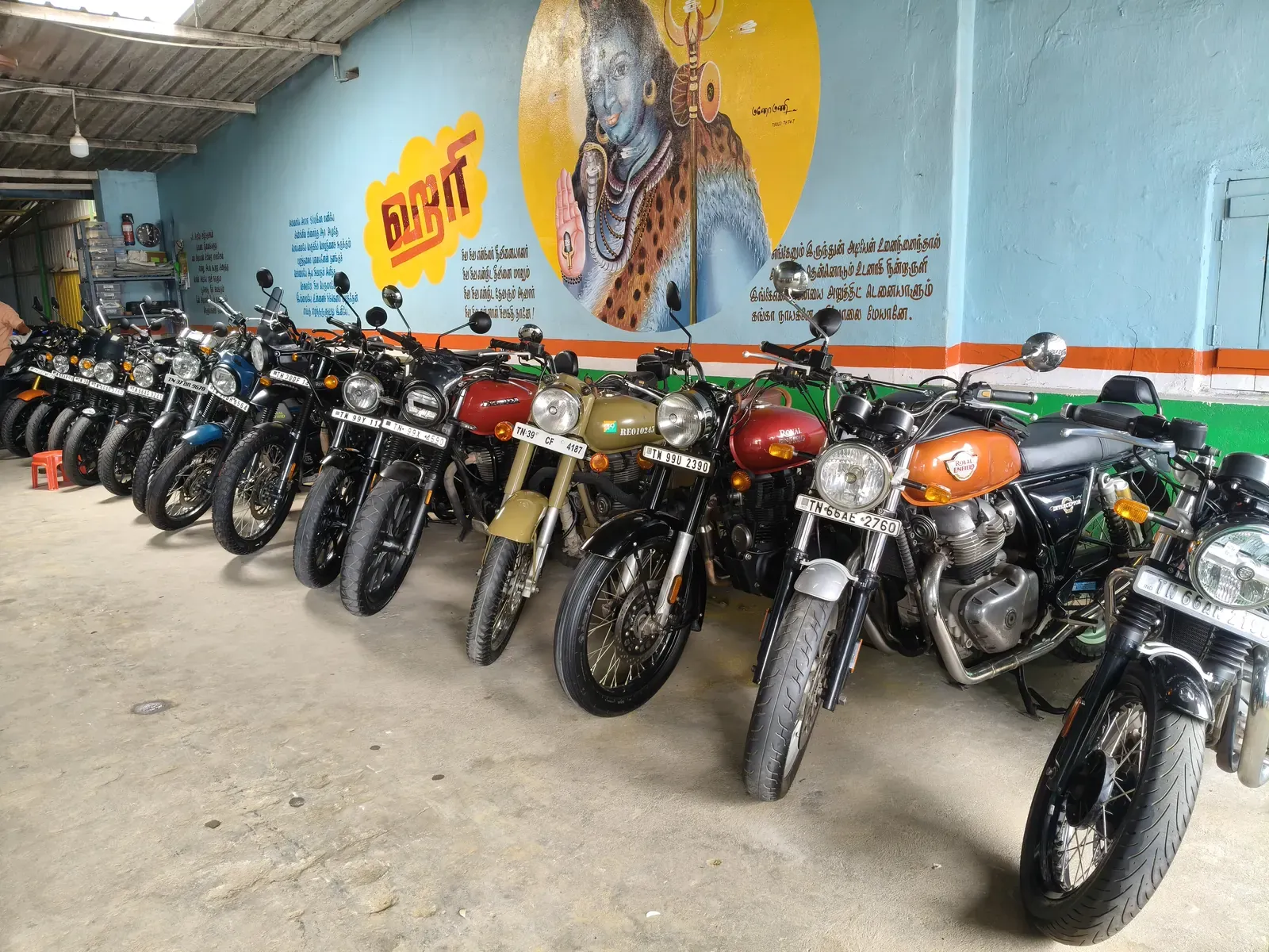Row of Royal Enfield and classic motorcycles under the HARI AUTO mural